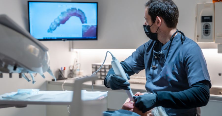 A Orthodontic Technologies, dentist scanning a patient’s teeth with a digital intraoral scanner while real-time 3D images display on the screen.