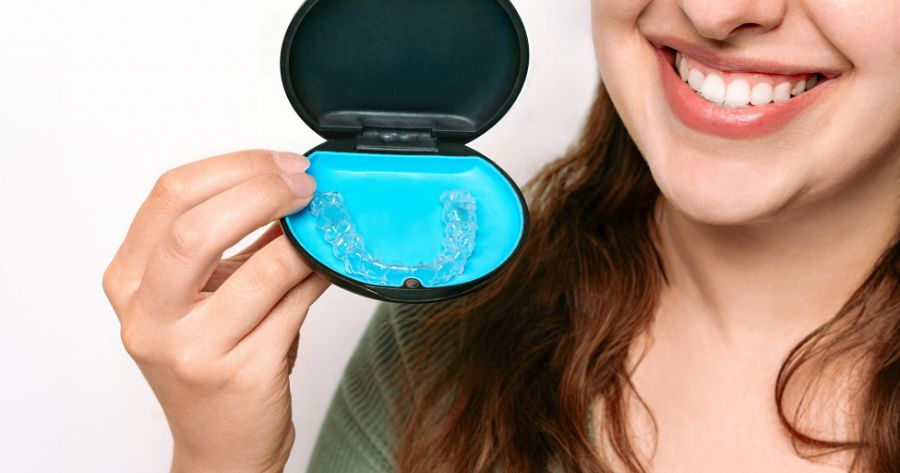 A smiling patient holding a case containing clear aligners, demonstrating modern invisible orthodontic treatment options.